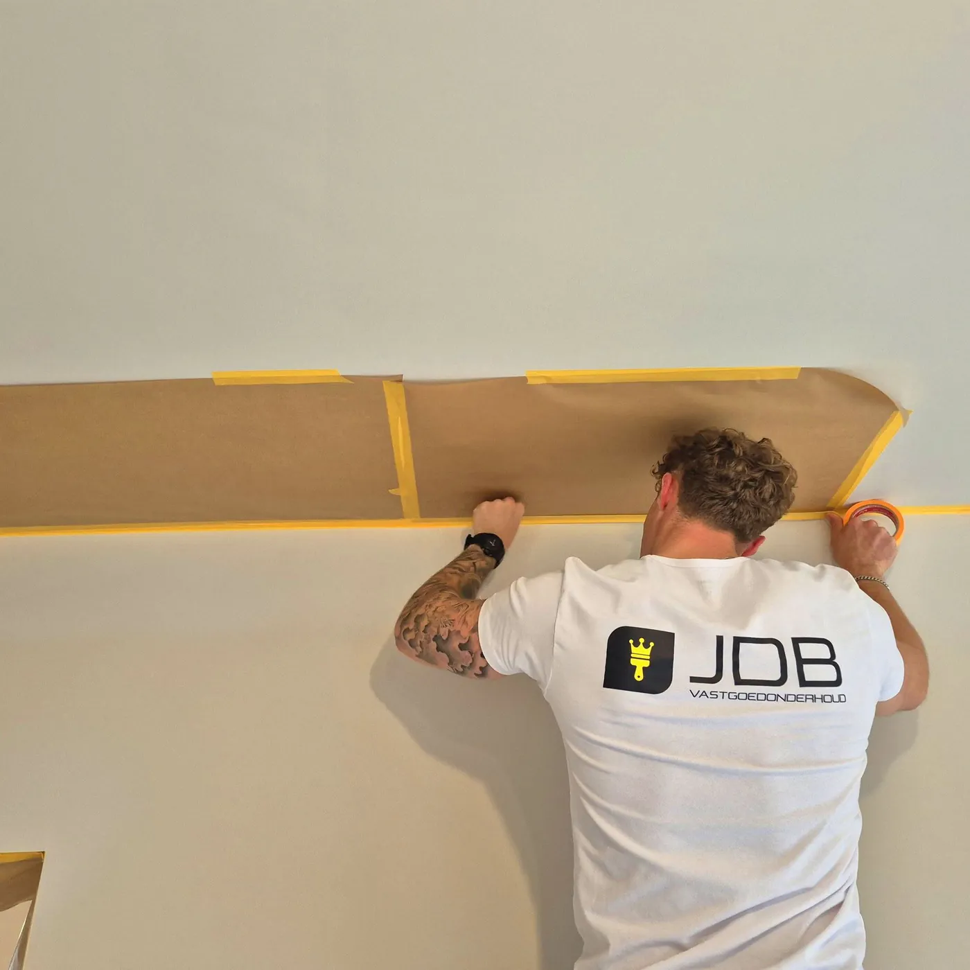 Schilder van JDB Vastgoedonderhoud plakt een wand af